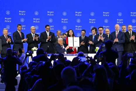 Trump holds up a signed "Board of Peace" charter as world leaders applaud behind him