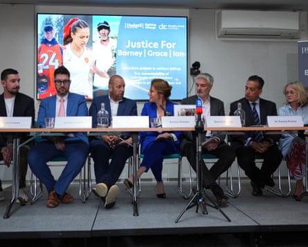 The families of the victims sit at a long table with name cards in front of them. Behind them on a screen are pictures of Ian Coates, Barnaby Webber and Grace O’Malley-Kumar and the words ‘Just for Barnaby, Grace, Ian’