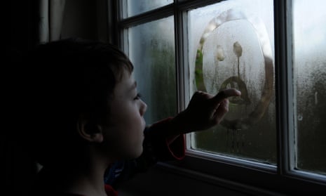 A child draws a sad face on a window