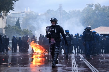 A police officer covered in paint walks near a fire during a demonstration against the "high cost of living", in Montpellier, southern France.