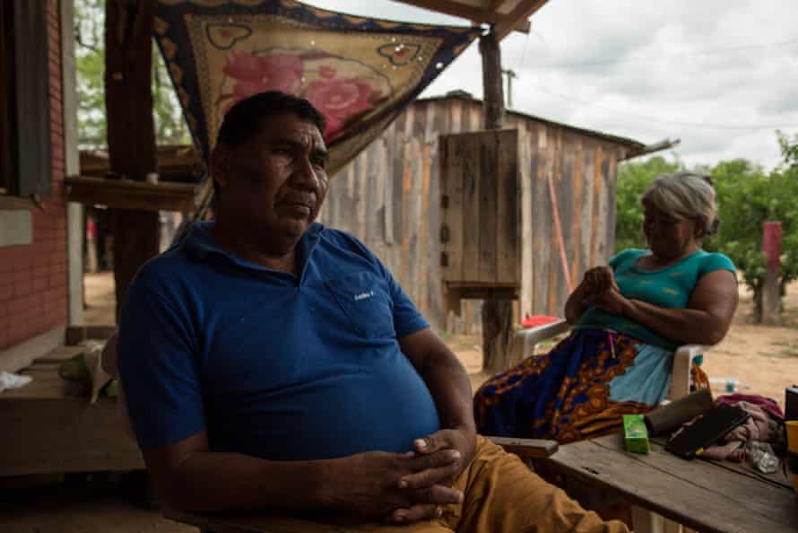 A man sits outside a small house with a woman with a wooden shack in the background