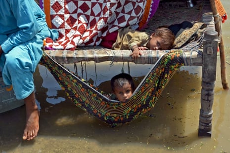 Children sit on a charpai surrounded by flood water several inches deep.