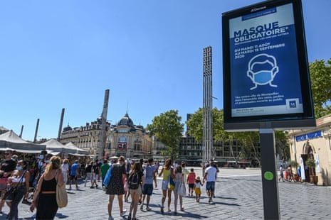 People wearing face masks walk next to a billboard reading ‘Mandatory mask in downtown Montpellier’, on 14 August 2020, in Montpellier, southern France.