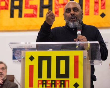 Rehman speaking at a lectern with the words ‘¡No Pasaran!’
