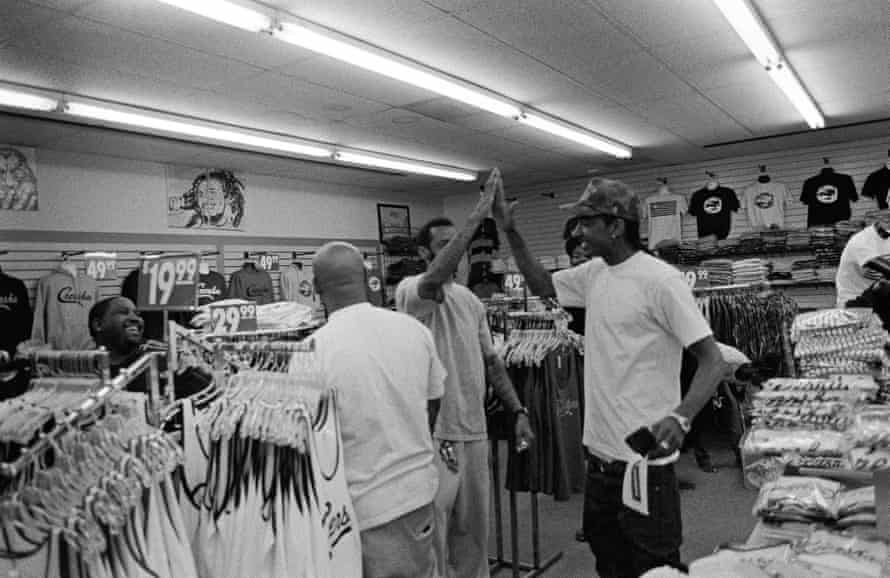 Two men clap hands in the middle of a clothing store in this black and white photo.