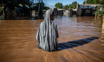 A woman wading through brown flood water in a residential area