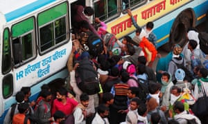 A crowd of people surrounding the entrance to a bus with someone on board trying to reach down to help someone in the crowd up