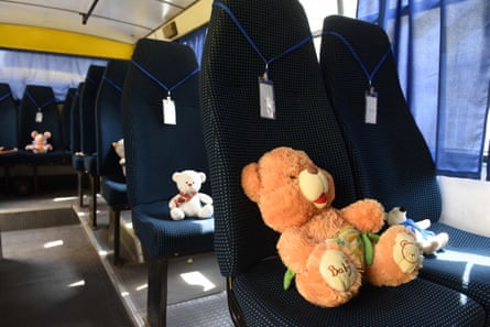 Soft toys sit on bus seats; each seat has a lanyard with a neame on it hanging on the headrest.