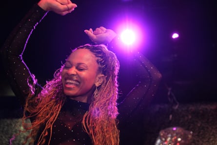 A black woman smiles and throws her arms in the air while dancing in a club.