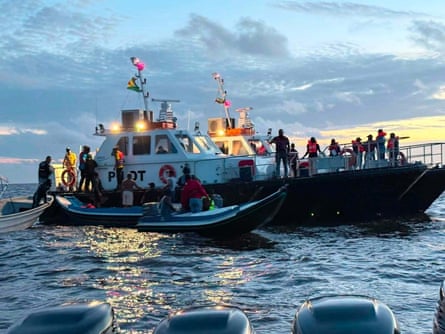 Two white boats carrying rescued passengers, with several smaller rescue vessels in the water beside it