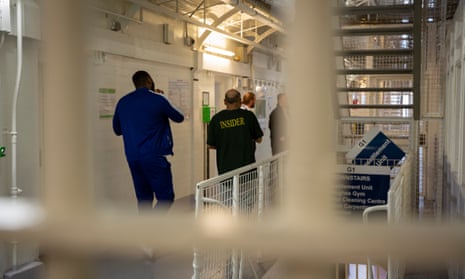 Two male prisoners walk down the landing towards to prison officers