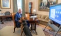 Joe Biden, in a suit and tie, sitting on a leather chair at a desk in an office with his hand on the head of Commander, the secret service dog.