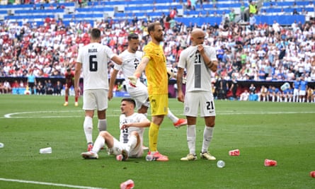 Dejected Slovenia on the pitch amid empty beer cups thrown on the pitch by fans.