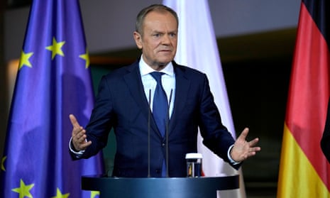 Donald Tusk stands at a podium, his arms outstretched.