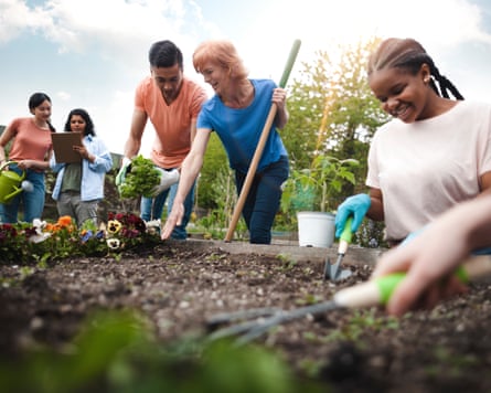 Multiracial group of young men and young women gather as volunteers to plant flowers in community garden with mature woman project manager advice and teamwork