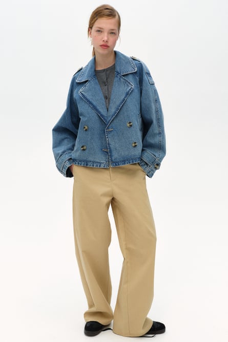 A model wearing a denim blue cropped trench coat and beige trousers