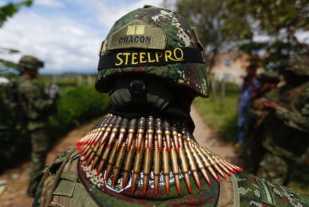 Soldier with a camouflage helmet and rows of bullets around his shoulders, seen from the back