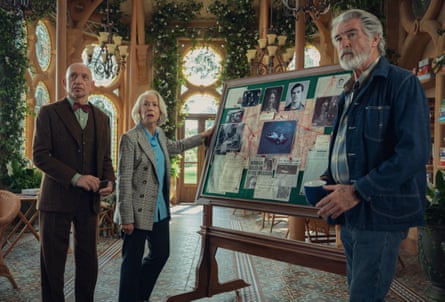 Kingsley, Mirren and Brosnan stand in an elaborate conservatory, with a corkboard bearing photos, maps, news articles etc linked with red thread