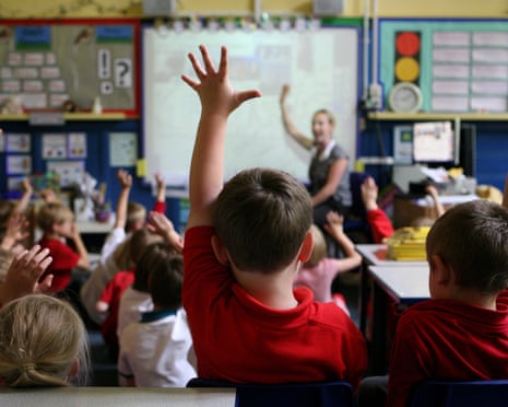 Primary school children in a classroom raise their hands