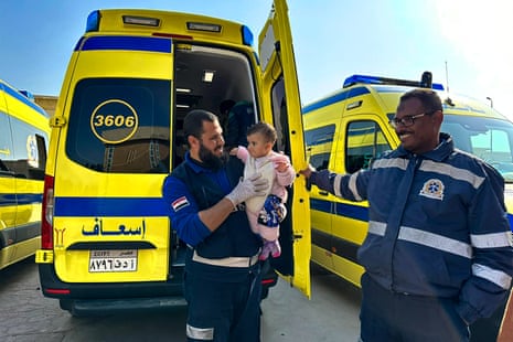 An Egyptian paramedic holds a Palestinian child as another paramedic holds open the door of a medical van