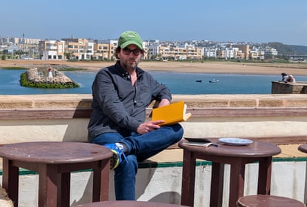 A man sitting at a table on the seafront with a book