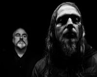 A black and white photo of Godflesh, with Ben Green in the background and Justin Broadrick in the foreground
