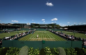 Blue sky over Wimbledon as people watch a doubles match on one of the outside courts