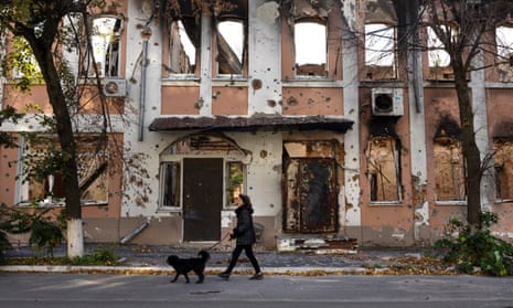 A woman walks her dog outside a destroyed building on 3 October 2022 in Izium, Ukraine.
