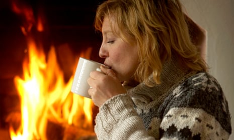 Young woman sitting in front of a fireside on a carpet and is drinking tea