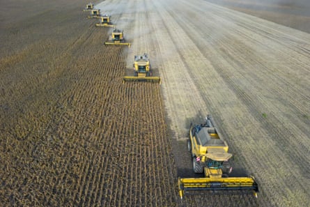 Five harvesters plowing through a vast field