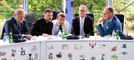 Donald Tusk, Volodymyr Zelenskyy, Emmanuel Macron, Keir Starmer and Friedrich Merz sitting at a table around a phone