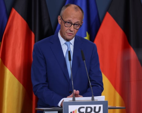 Friedrich Merz speaks into microphones at a lectern, with German flags behind him