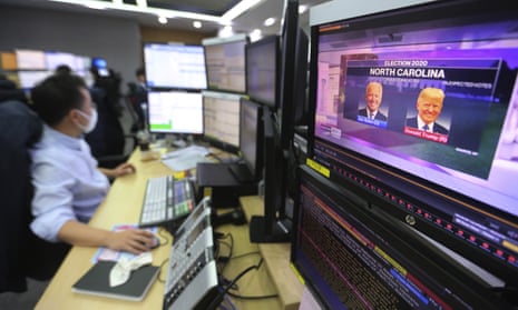 A screen shows live broadcasting of a news programme on the US elections as a currency trader works in a foreign exchange dealing room