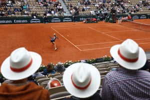Three spectators wearing matching hats watch a tennis match