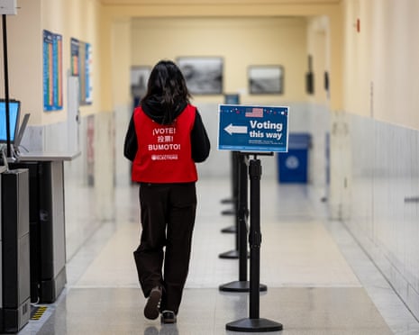 A person wearing a red vest that says 'vote' in multiple languages walks in a corridor