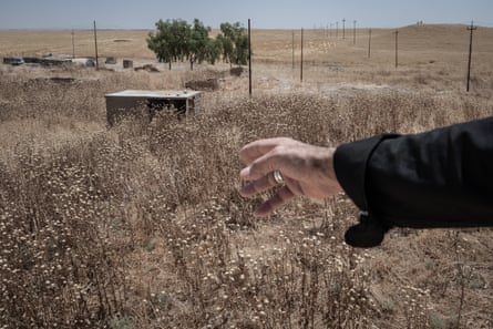 A hand points to an abandoned building in an overgrown dry landscape