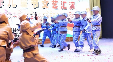 Small children dressed in replica uniforms pretend to fire guns at each other on a stage.