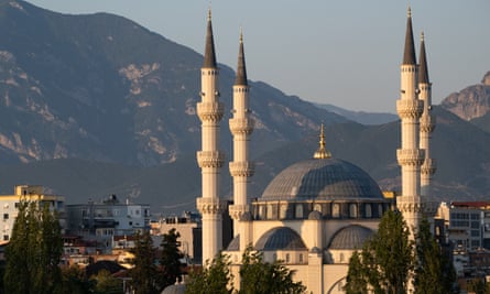 The mosque is lit in evening sunlight, with mountains in the background.