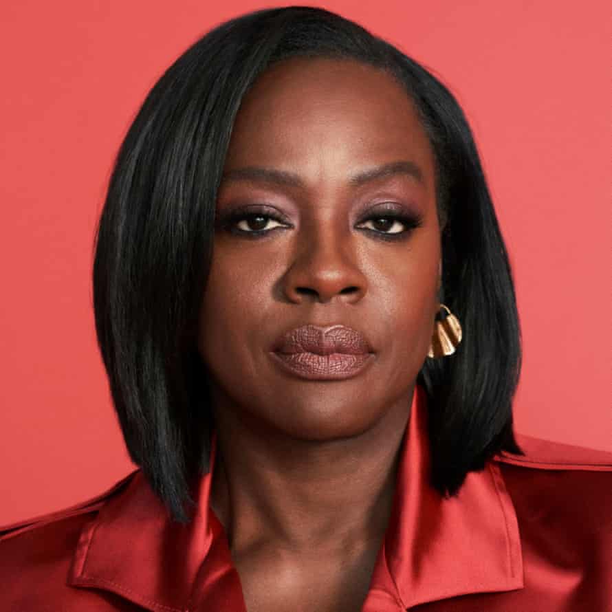 A portrait of Viola Davis wearing an orange satin coat against an orange background