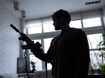 A man holding an battle firearm silhouetted against a window