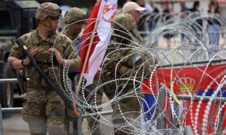 US K-For soldiers behind barbed wire carrying guns in front of Serbian supporters.