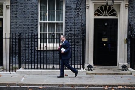 he is pictured as a small figure walking away down the street with the door of No 10 behind him. He wears a dark blue suit and has documents under his arm, and is smiling.