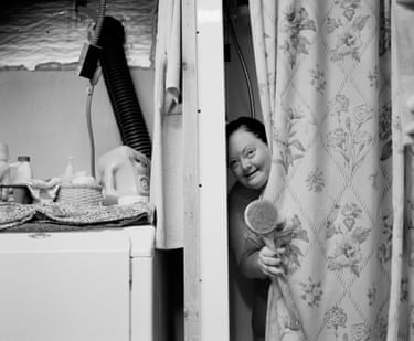 A woman with down’s syndrome looks out from behind a curtain.