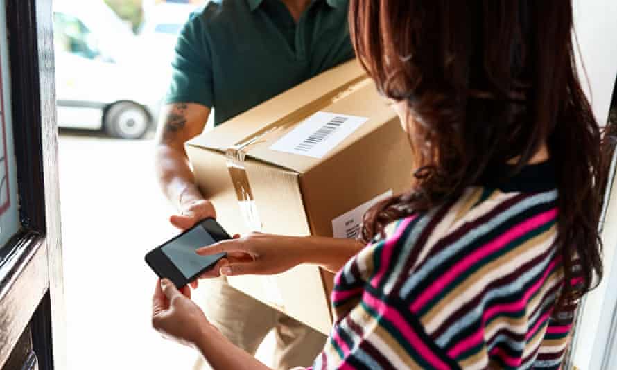 Female customer at front door holding smartphone and receiving package from delivery man
