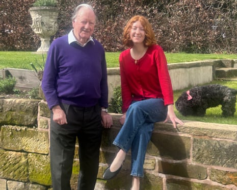 A grandfather and granddaughter by a wall with their dog