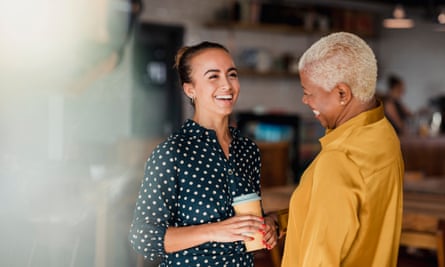 Enjoying Their Breaks TogetherPosed by models Two women laughing while standing in a cafe at their workplace. One of the women is holding a take out hot drink cup.