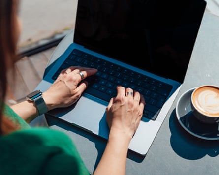 Over the shoulder view of a woman’s hands typing on a laptop keyboard, working at cafe while enjoying coffee