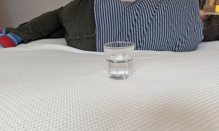 A glass of water balanced on a mattress that a man is laying on