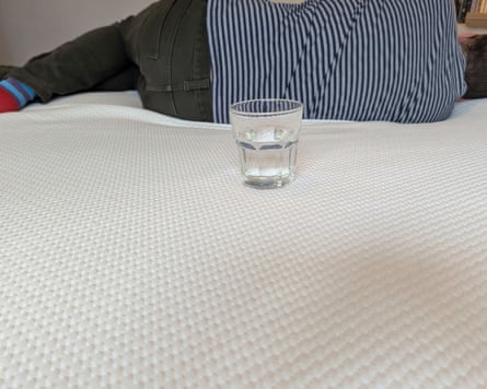 A glass of water balanced on a mattress that a man is laying on