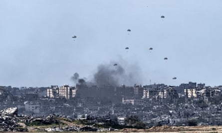 Humanitarian aid packages fall on Gaza as smoke rises on 7 March.